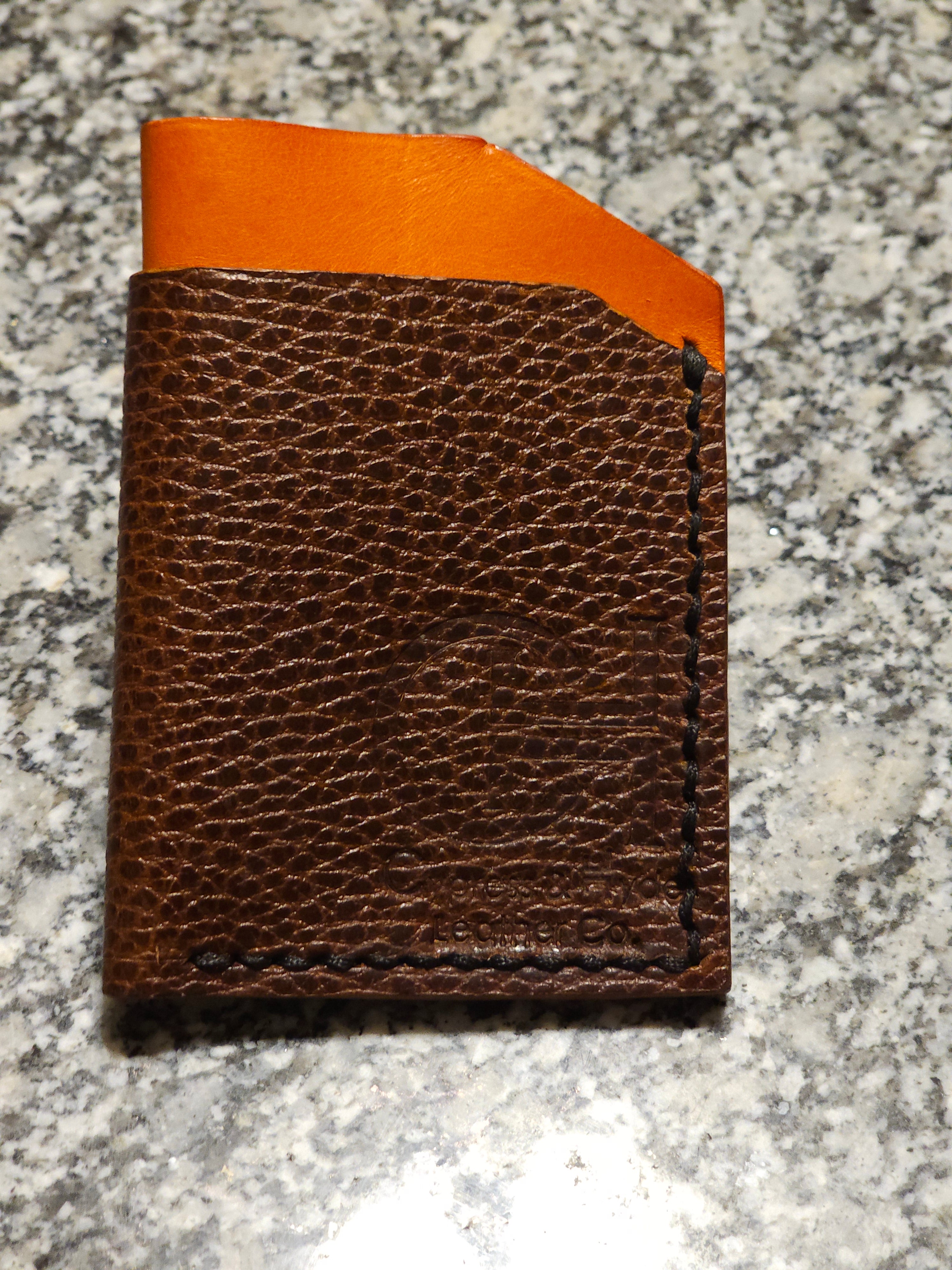 Brown leather wallet with orange top corner on a wooden surface