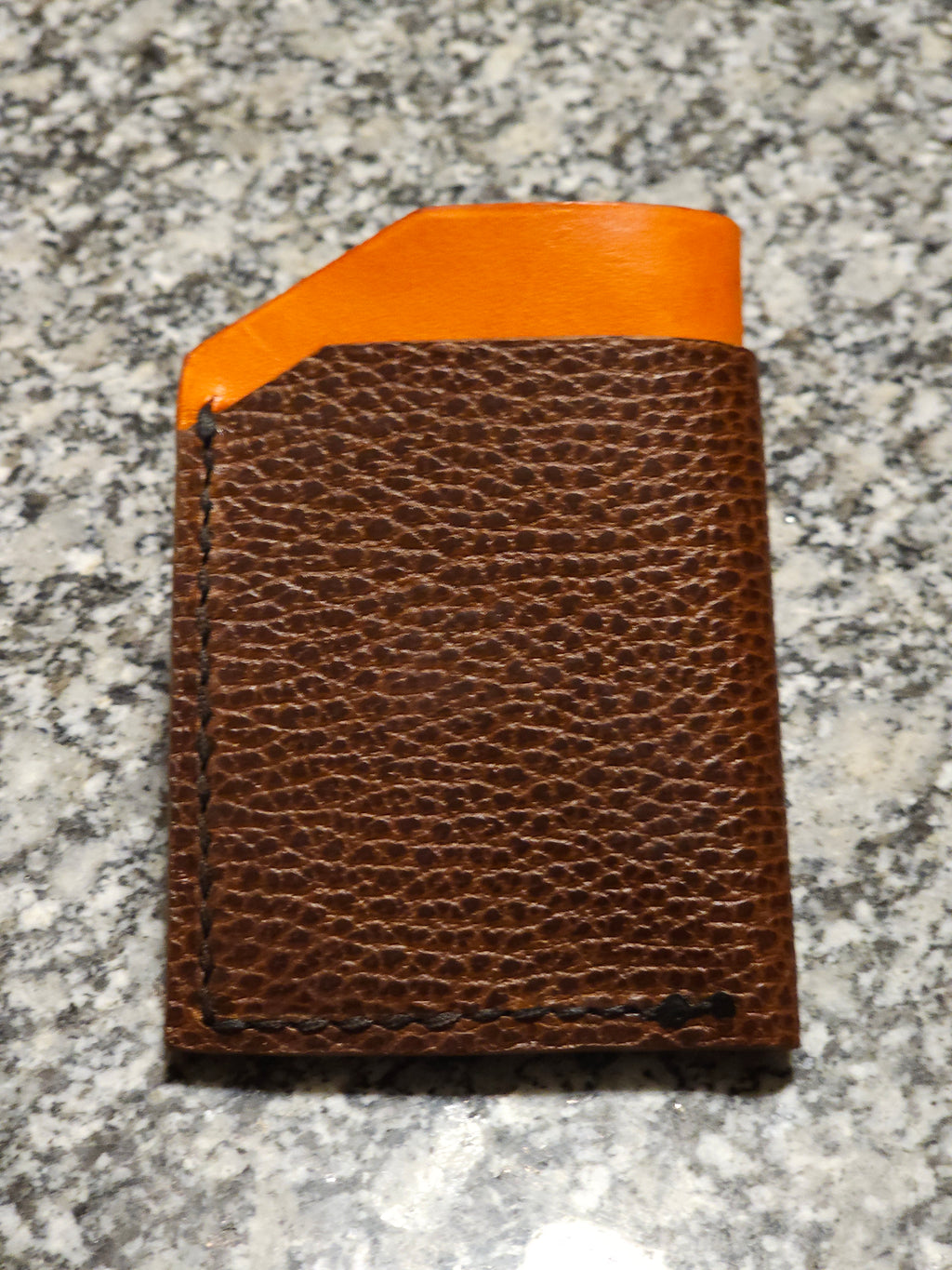 Brown leather wallet with orange interior on a gray surface